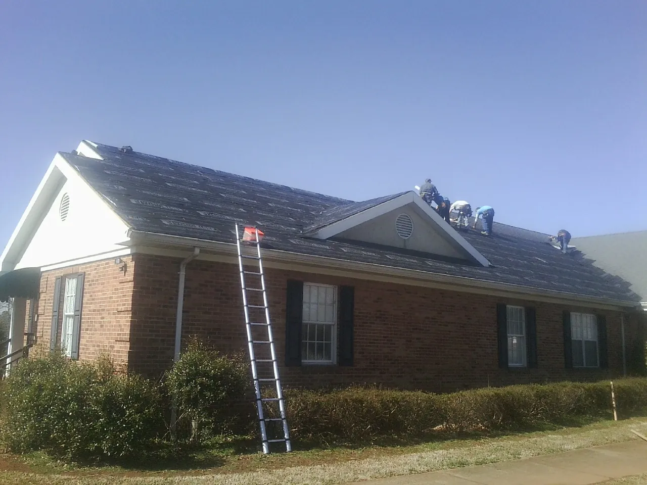 Crew tearing shingles off a brick ranch roof with a ladder set — Metal Roof Repair work by our crew in Clackamas