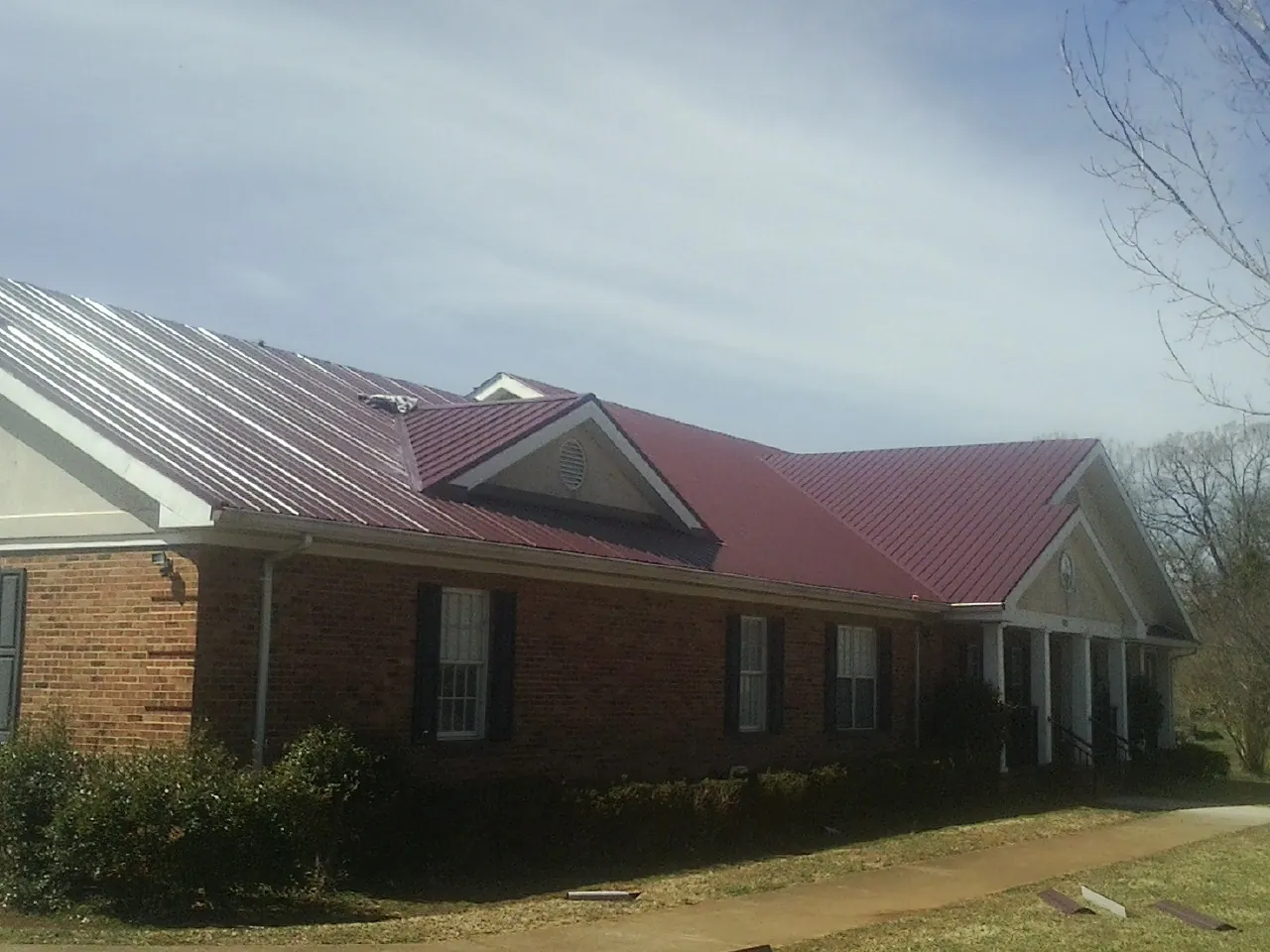 Red metal roof with gabled entries on a long brick building, from a Hail Damage Roof Repair job in Clackamas