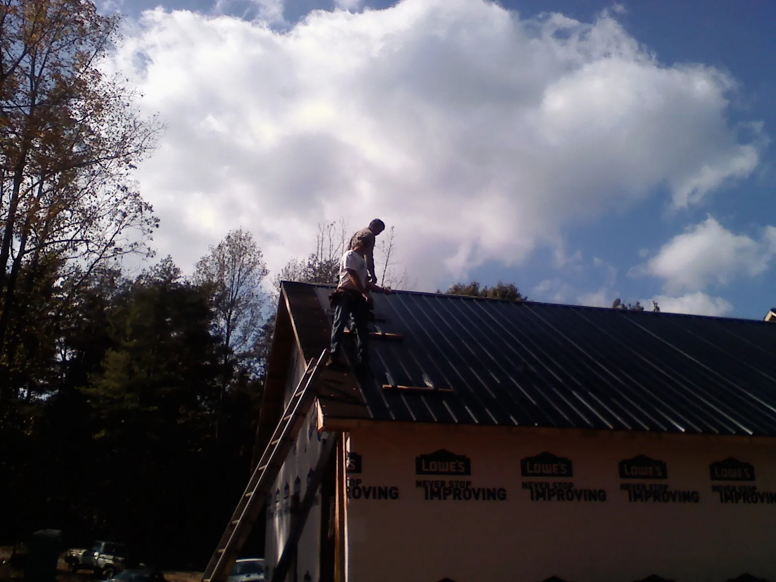 Roofer fastening dark metal panels high against a cloudy sky, from a Roof Inspection job in Clackamas